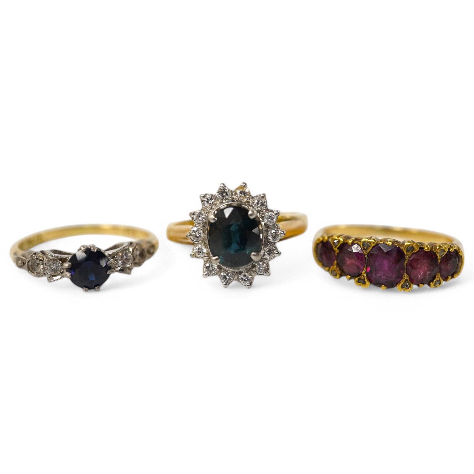 A group of three rings, comprising: a sapphire and diamond cluster ring, size M1/2, stamped 14K and 585; a five-stone ring set with cushion-shaped garnets and rose-cut diamonds, size L; and a synthetic sapphire and simul